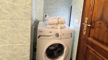Een compacte, witte wasmachine voor eigen gebruik met een bedieningspaneel, een handdoek erboven en een houten deur aan de rechterkant.