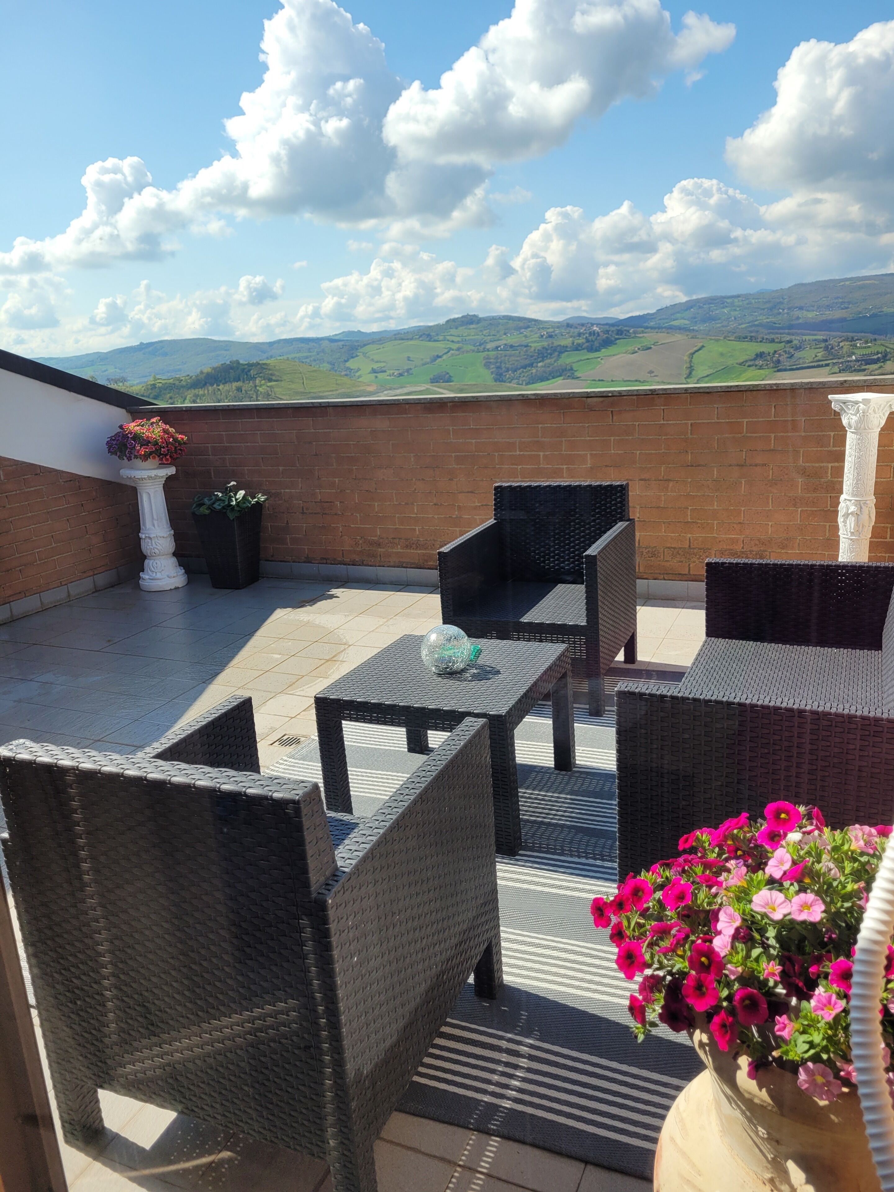 A terrace with wicker furniture, a potted plant, and a view of green hills.