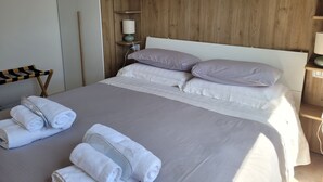 Una cama bien hecha con almohadas, un cabecero de madera, una mesita de noche con una lámpara y toallas enrolladas en el suelo.