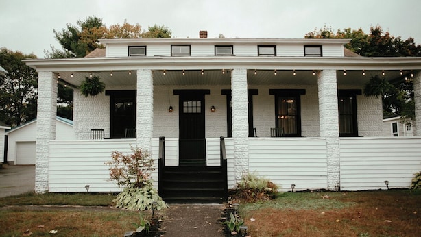 A white two-story house with a front porch, columns, and a small garden. - Charming 4-bedroom house in enchanting Millinocket with AC, WiFi (Millinocket)