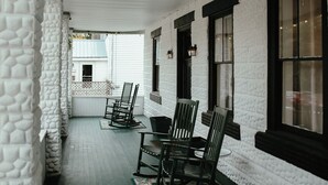 A covered porch with white walls and dark wooden shutters, featuring several rocking chairs and a small table. - Charming 4-bedroom house in enchanting Millinocket with AC, WiFi (Millinocket)