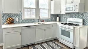 A kitchen with white cabinets, a microwave, a stove, and a dishwasher. There are two windows with a view of trees outside. - Charming 2-bedroom house in serene Coloma with AC, WiFi (Coloma)