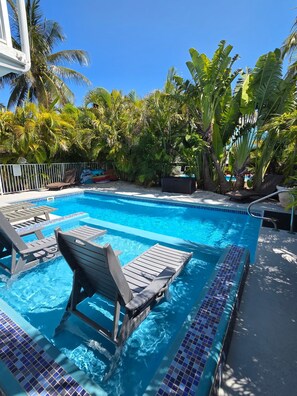 A swimming pool with lounge chairs, surrounded by tropical plants and a clear blue sky.