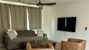 A living room with a sofa, two armchairs, a coffee table, a ceiling fan, and a flat-screen TV mounted on the wall. - Charming 3-bedroom House in Queen Creek w/ Community Pool (Queen Creek)