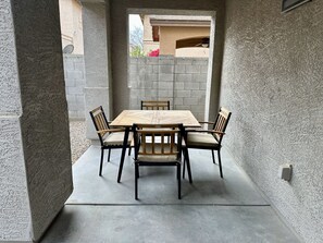 A patio with a wooden table and chairs, surrounded by stone walls. - Charming 3-bedroom House in Queen Creek w/ Community Pool (Queen Creek)