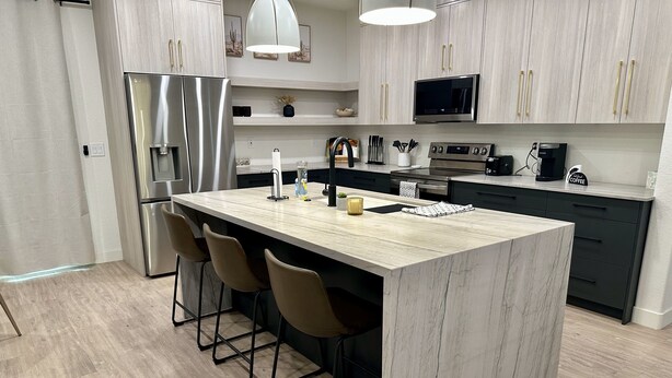 A modern kitchen with a central island, bar stools, a refrigerator, a microwave, a coffee machine, and a TV. - Charming 3-bedroom House in Queen Creek w/ Community Pool (Queen Creek)