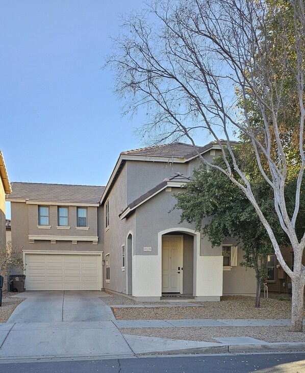 A two-story residential building with a garage, a front door, and a small tree in the yard. - Charming 3-bedroom House in Queen Creek w/ Community Pool (Queen Creek)