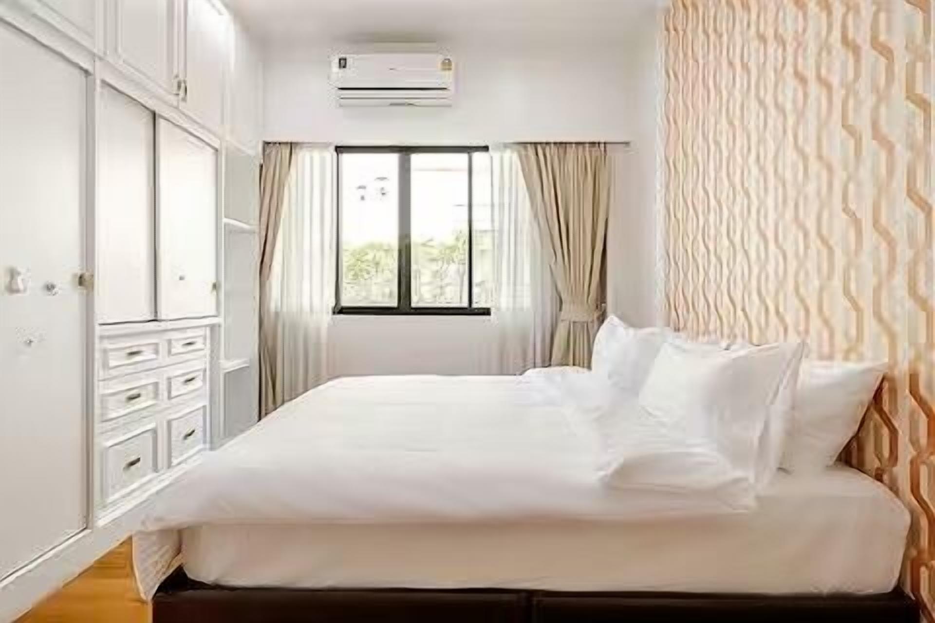 Un lit bien fait dans une chambre d’hôtel, avec une fenêtre, des rideaux et un appareil de climatisation.