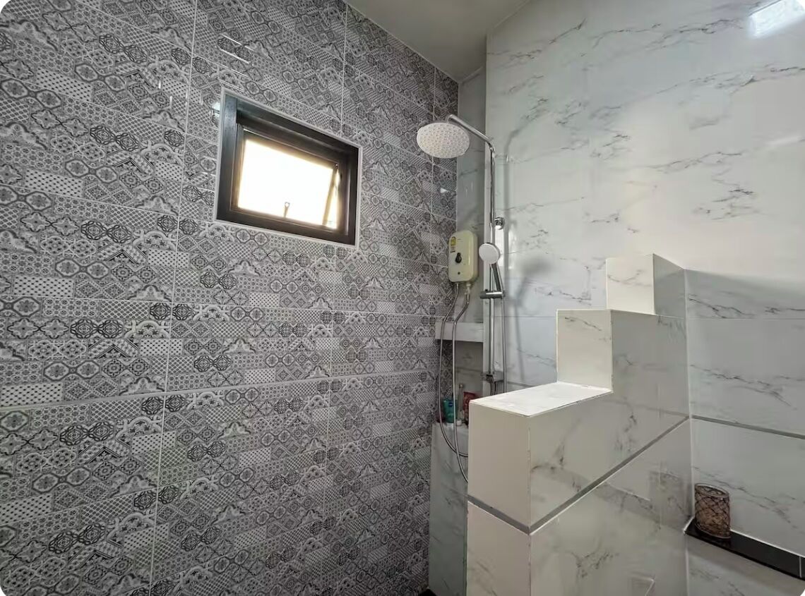 Ein Badezimmer mit gemusterten Fliesen, einer Dusche und einem Fenster.