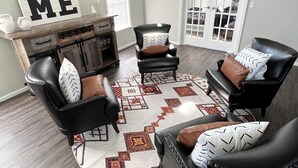 Un salon comprenant trois fauteuils en cuir noir, un meuble en bois et un tapis à motifs géométriques.