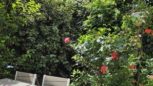 Terrassa amb jardí, taula i cadires, envoltada de vegetació exuberanta i plantes en flor.