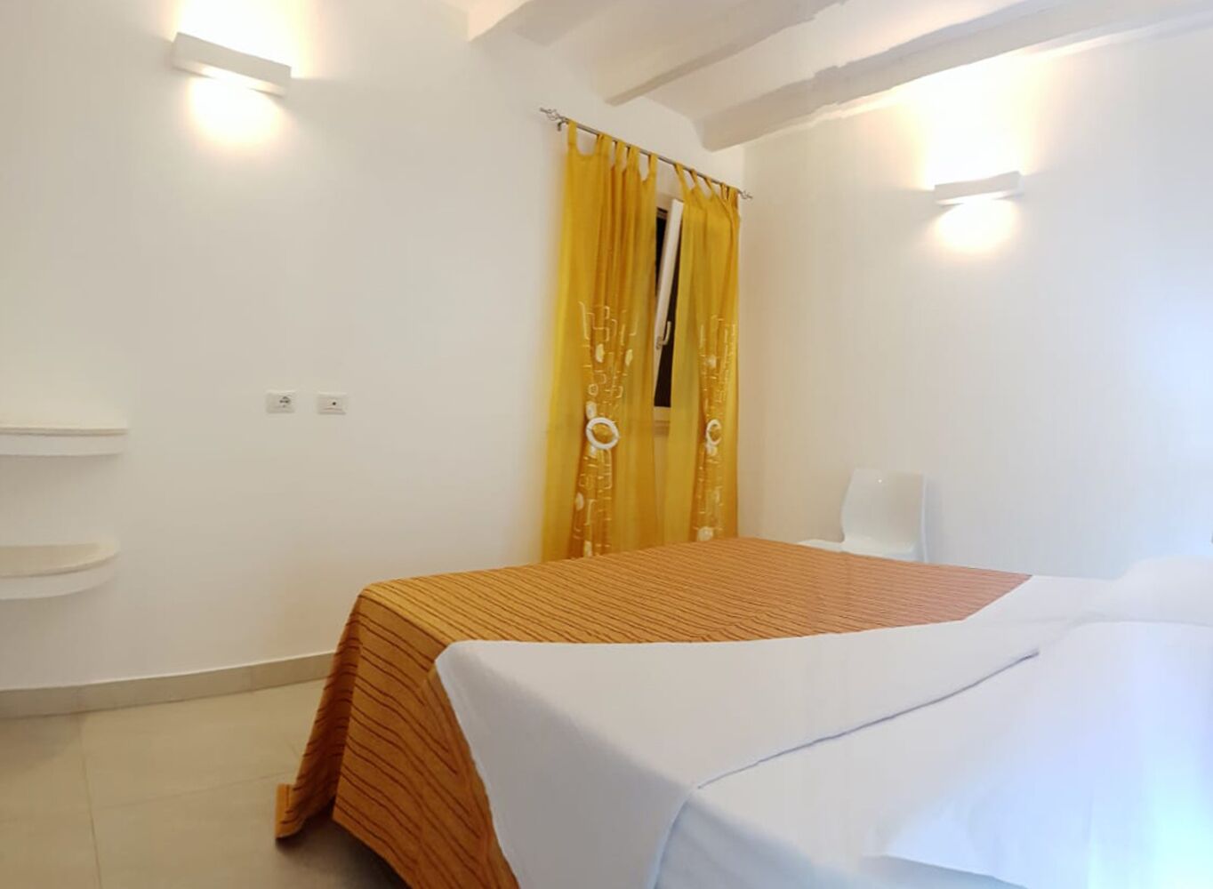 Une chambre à coucher avec un lit, une fenêtre ornée de rideaux jaunes et un mur blanc.