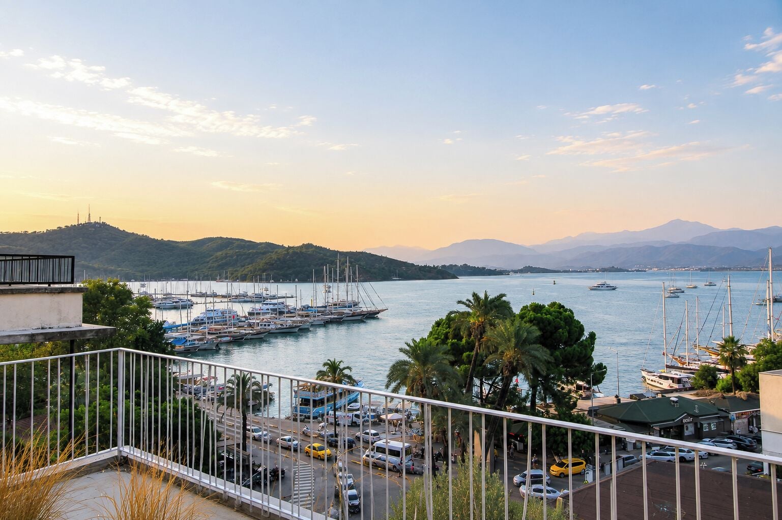 Un puerto deportivo con barcos amarrados, un aparcamiento y vistas a las colinas en la distancia.