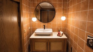 A bathroom with a wooden door, a white sink, a round mirror, and two wall-mounted lights. - Roof Rooms Fethiye (Fethiye)