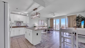 A modern kitchen with white cabinetry, a central island, and a dining area with white chairs and a table. - Laketown Wharf 1116 (Panama City Beach)