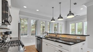 A modern kitchen with white cabinetry, a black granite countertop, stainless steel appliances, and pendant lighting. - Beach, Please (Santa Rosa Beach)