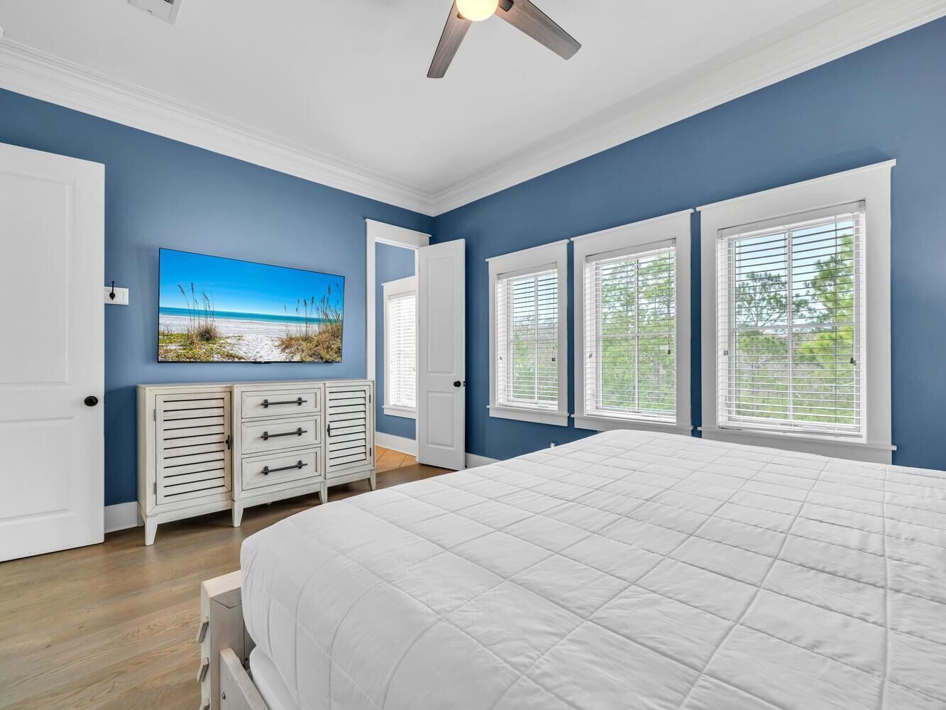 A bedroom with a large bed, white dresser, and a painting of a beach scene.