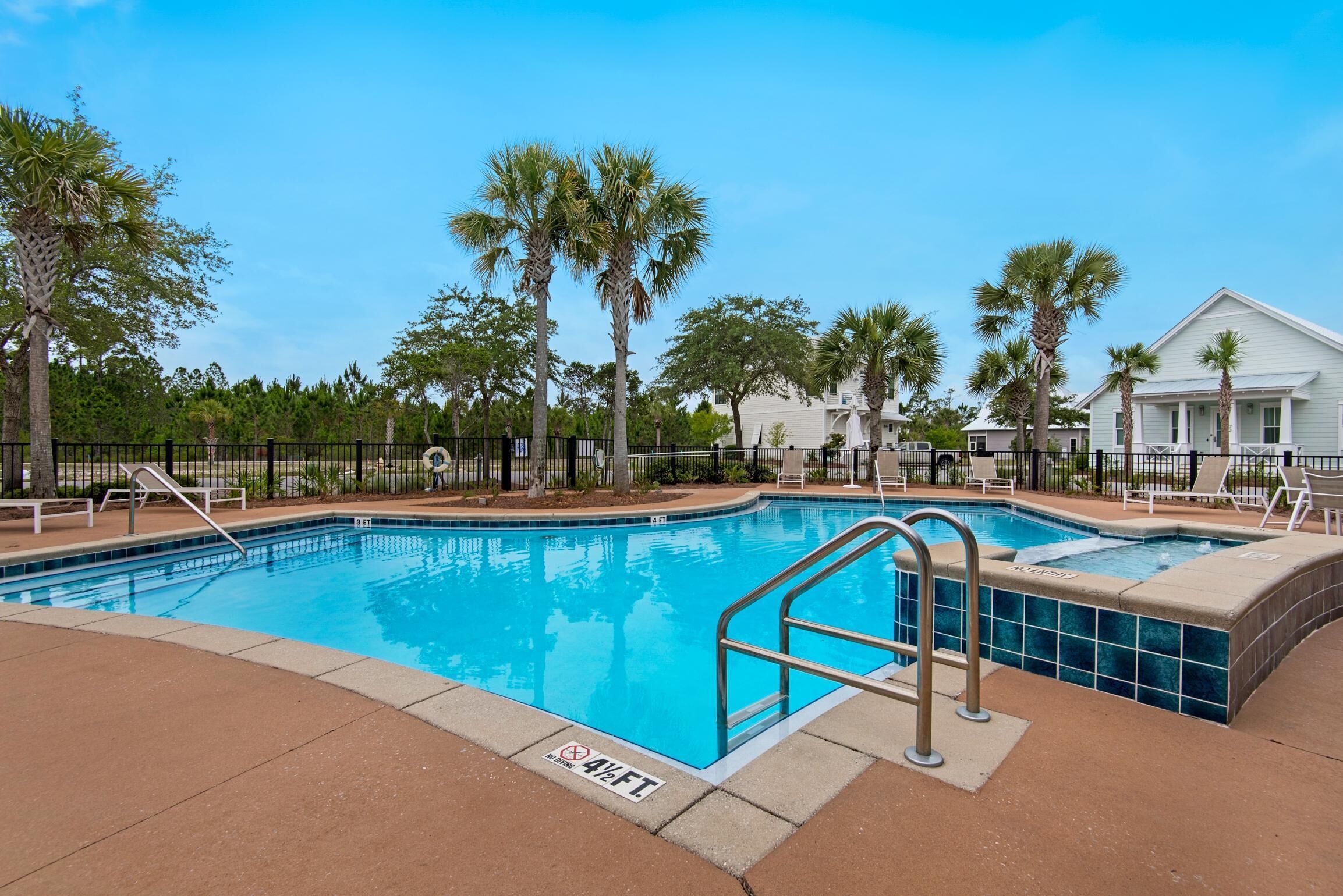 A swimming pool with a 4½ ft depth, surrounded by palm trees and a fence, with a clear blue sky above.