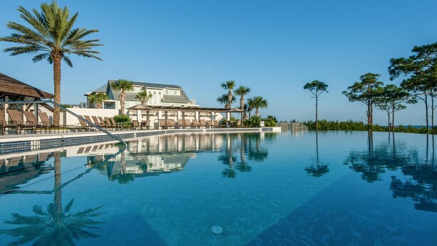 A hotel with a large infinity pool, palm trees, and a clear blue sky. - Beach, Please (Santa Rosa Beach)