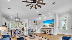 A spacious living room with a wooden coffee table, blue sofas, a staircase, and a large TV on the wall. - Beach, Please (Santa Rosa Beach)