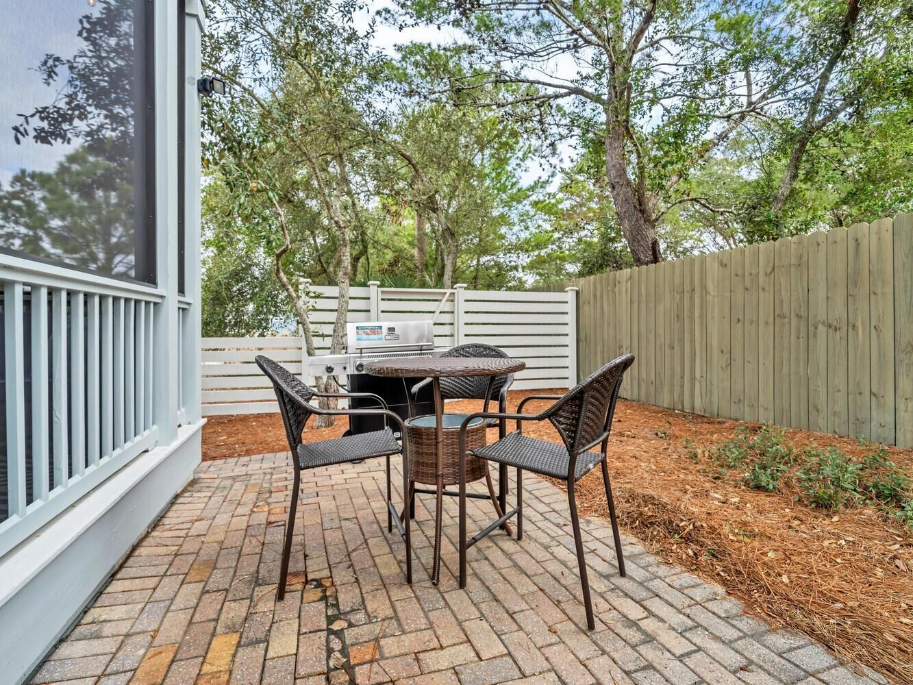 An outdoor patio with a brick floor, a round table, and four wicker chairs.