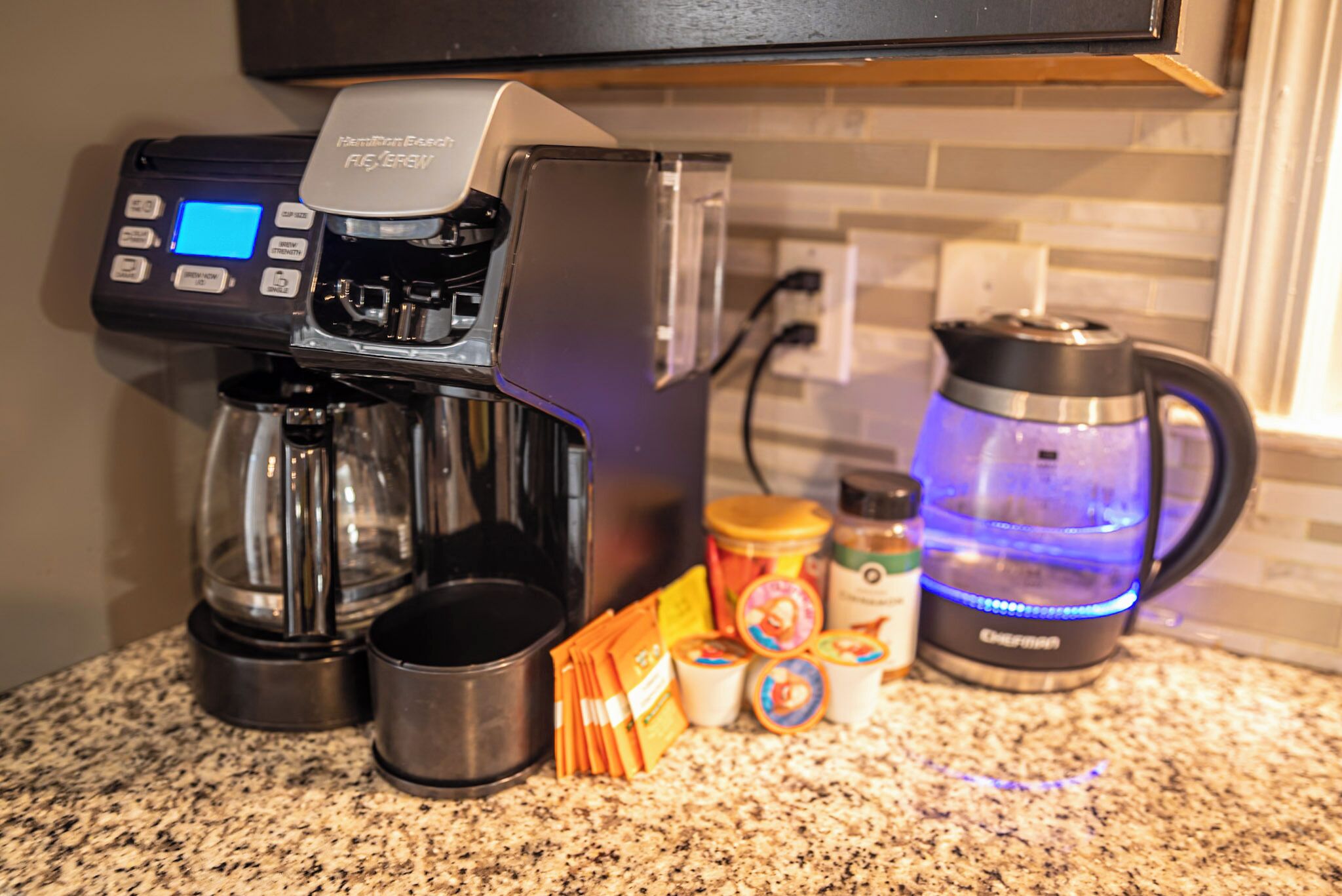 A coffee machine with a digital display, a kettle, and various coffee pods on a kitchen counter.