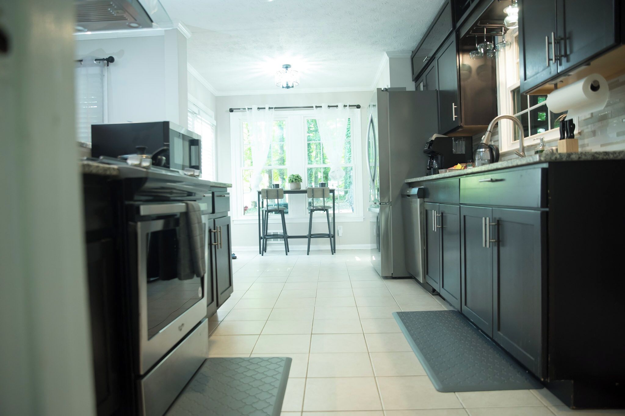 A modern kitchen with stainless steel appliances, a dining area with two chairs, and a view of greenery outside.
