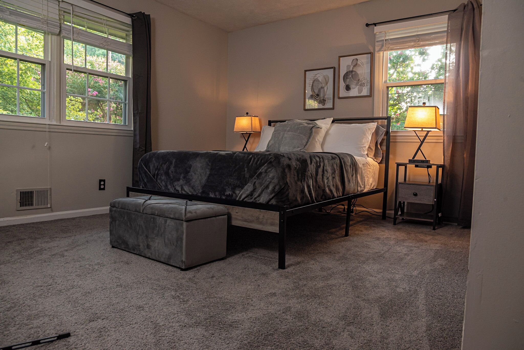 A bedroom with a bed, two bedside tables with lamps, a window, and a radiator.