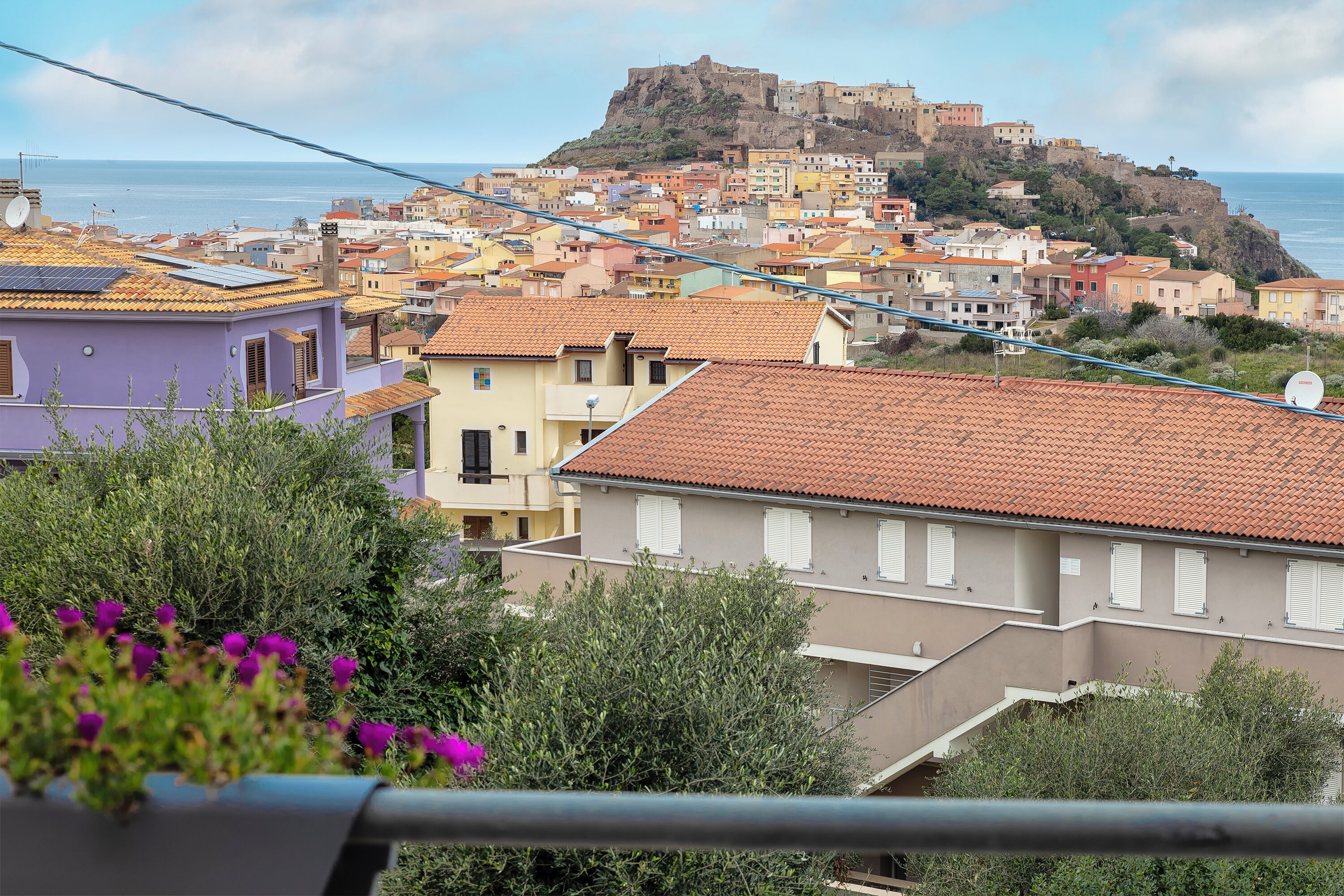 A coastal town with colorful buildings, a prominent hilltop structure, and a view of the sea.