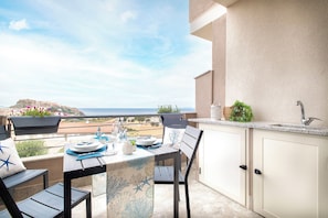 Un balcon avec une table dressée pour les repas, une chaise, un évier et une vue sur la mer.