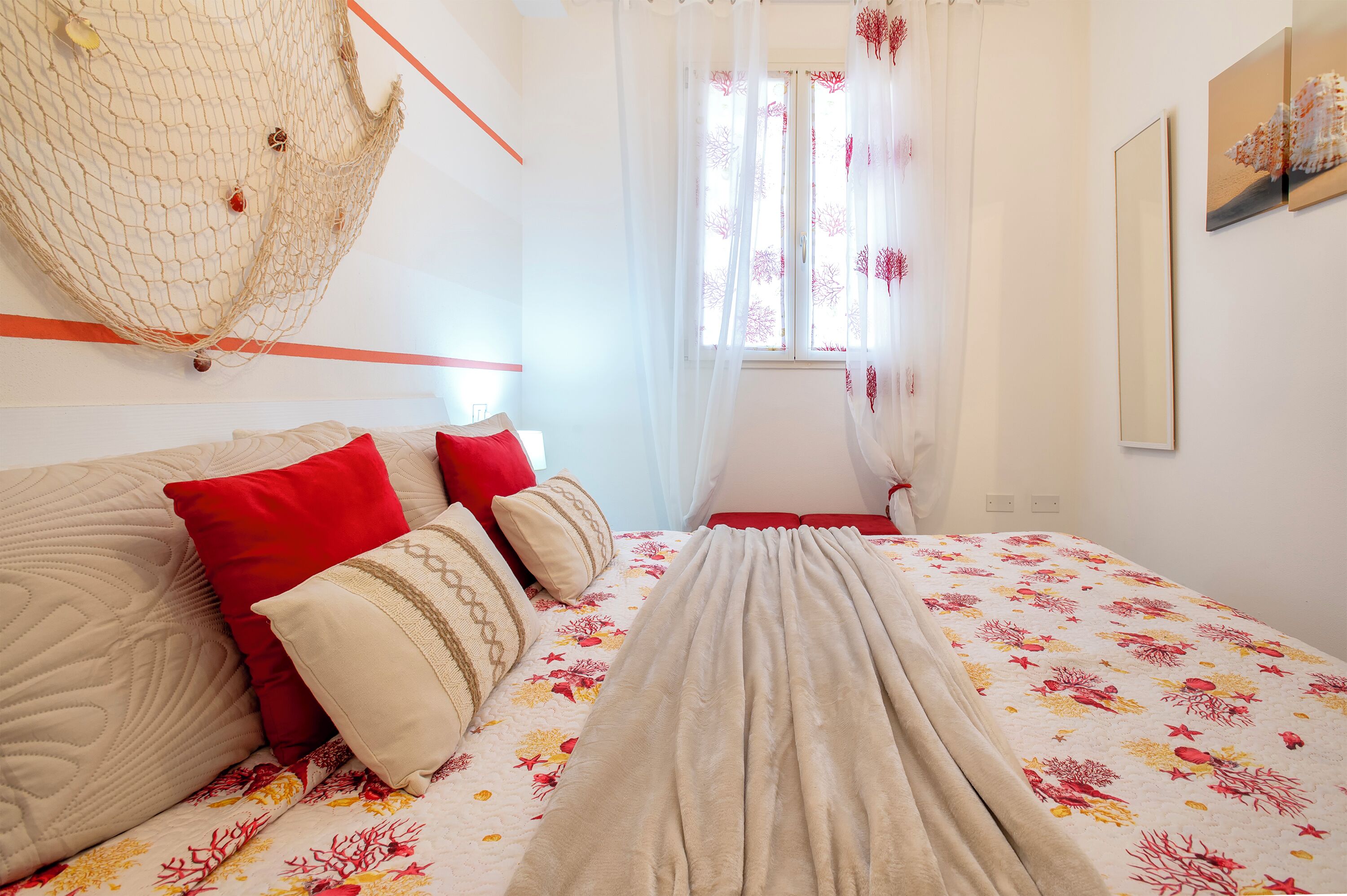 A neatly made bed with floral bedding, a hanging net, and a window with sheer curtains.
