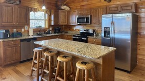 A wooden cabin kitchen with granite countertops, stainless steel appliances, and a deer head mounted on the ceiling.