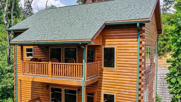 A two-story log cabin with a balcony on the upper floor and a stone foundation.