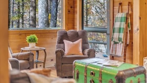 Ein gemütliches Blockhaus-Interieur mit einem Ledersessel, einem kleinen runden Tisch mit einem Blumentopf und einem grünen Koffer.