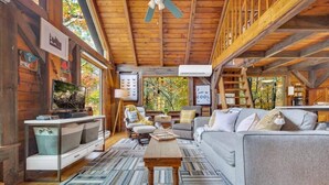 A cozy cabin interior with a wooden ceiling, a television, a sofa, and a dining area.