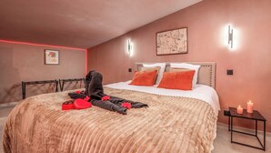 Une chambre à coucher avec un grand lit, une tête de lit, une table de chevet avec des bougies et un luminaire fixé au mur.
