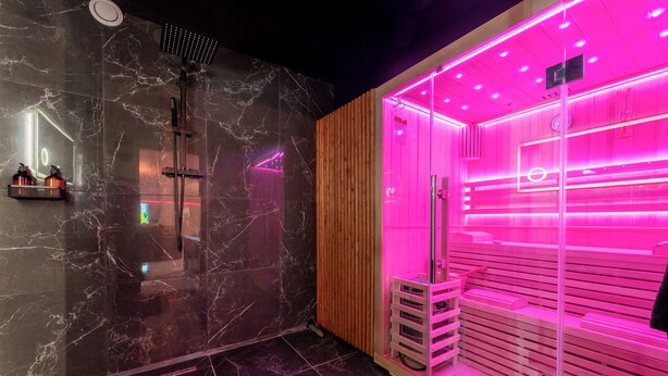Une salle de bain moderne avec un mur en marbre, un panneau en bois et un hammam éclairé en rose.
