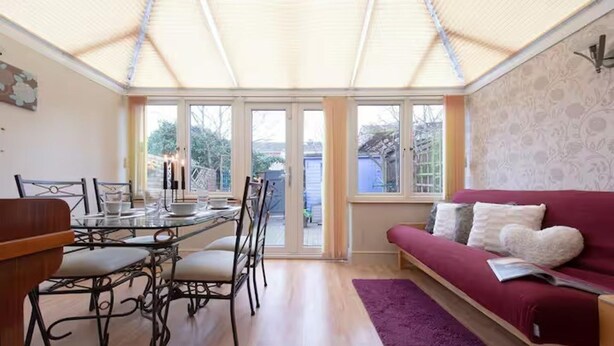A dining area with a glass table and chairs, a red sofa, and a purple rug. - 3bedroom Sleeps8 Parking Familyfriendly Nearexcel (London)