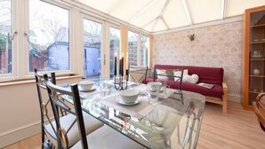 A conservatory with a glass dining table, a red sofa, and a bookshelf. - 3bedroom Sleeps8 Parking Familyfriendly Nearexcel (London)