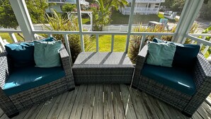 A covered outdoor seating area with wicker furniture and cushions, overlooking a residential neighborhood with houses and greenery. - Charming 2 BR cottage in Great Guana Cay short walk to beach,  AC WiFi Generator (Great Guana Cay)