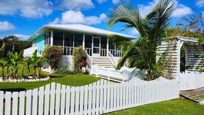 A house with a white picket fence, a covered porch, and a well-maintained lawn. - Charming 2 BR cottage in Great Guana Cay short walk to beach,  AC WiFi Generator (Great Guana Cay)