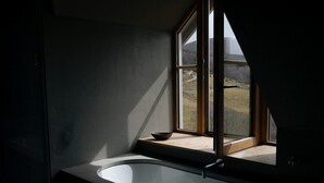 A modern bathroom with a freestanding bathtub, a window with a view of a landscape, and a small shelf with a bowl.