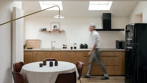 A modern kitchen with a round dining table, wooden cabinets, and a black refrigerator.
