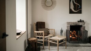 A cozy living room with a fireplace, a wooden chair, a small table, and a decorative mirror on the wall.