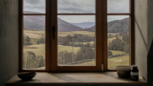 A room with a large window overlooking a rural landscape.