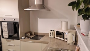 A modern kitchen with a stainless steel sink, a microwave, a toaster, and a range hood. - Cozy Apartment at Highbanks The Annex (Newhaven)