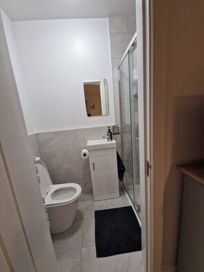 Casa de banho compacta com sanita, lavatório e cabine de duche em vidro.