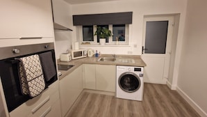 A compact kitchen with a washing machine, a microwave, a toaster, and a sink. - Cozy Apartment at Highbanks The Annex (Newhaven)