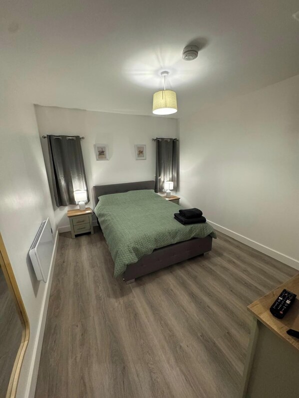 A bedroom with a bed, bedside tables, a lamp, a ceiling fan, and a remote control on a wooden side table. - Cozy Apartment at Highbanks The Annex (Newhaven)