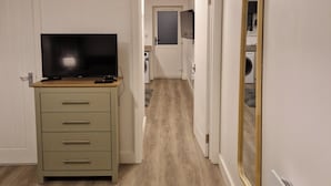 A hallway with a wooden floor, a television on a cabinet, a mirror on the wall, and a door leading to another room. - Cozy Apartment at Highbanks The Annex (Newhaven)